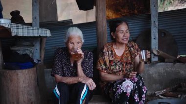 İki yaşlı Taylandlı kadın birlikte oturup kristal bardaklarda sıcak çay yudumluyorlar - 4K Yatay