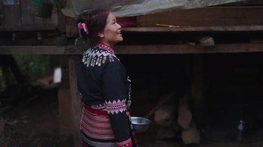 Geleneksel giyinmiş yaşlı Taylandlı kadın geleneksel ahşap bir evin önünde kaseyi tutarken mutlu bir şekilde gülümsüyor - 4K Yatay