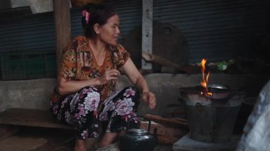 Vietnamlı bir kadın kırsal alanda geleneksel bir odun sobasını kullanarak sıcak bir içecek hazırlıyor - 4K Yatay