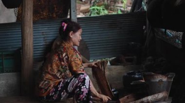 Deneyimli yaşlı kadın, sade mutfağın içinde odun kesiyor ve geleneksel yemek pişirme yakıtı hazırlıyor. 4K yatay.