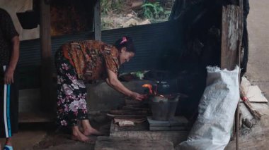 Köy ortamında geleneksel pişirme yöntemlerini gösteren bir odun sobasının üzerinde yemek hazırlayan yaşlı kadın - 4K Yatay