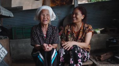 Yaşlı bir Asyalı kadın ve kızı birlikte oturmuş mütevazı bir geleneksel evde hikayeler ve kahkahalar atıyorlar - 4K Yatay