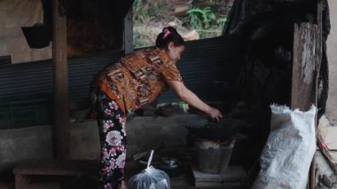 Asyalı kadın ahşap mutfakta geleneksel yemekleri dikkatlice pişiriyor. Klasik odun ateşi tavasını kullanıyor. 4K Yatay.