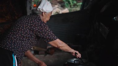 Yaşlı büyükanne kırsal bir mutfakta geleneksel yemek pişirme yöntemlerini kullanarak ev yapımı yemek hazırlıyor - 4K Yatay