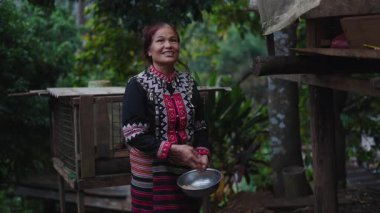 Geleneksel giysili Asyalı kadın günlük yaşamı gösteren kırsal bir ortamda tavuk yemi hazırlıyor - 4K Yatay