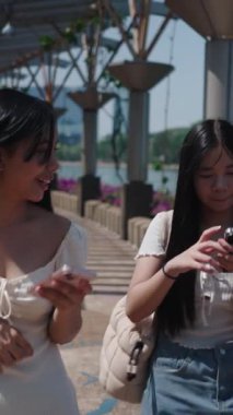 İki arkadaş birlikte yürüyorlar, aşağıya bakıyorlar, akıllı telefonlara dalmışlar, sosyal medyada geziniyorlar.