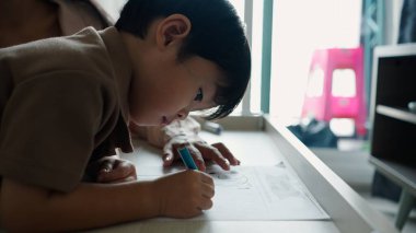 Genç bir öğrenci, mavi kalemle resim çizerken masa başında oturmuş, aktiviteleri öğreniyor.