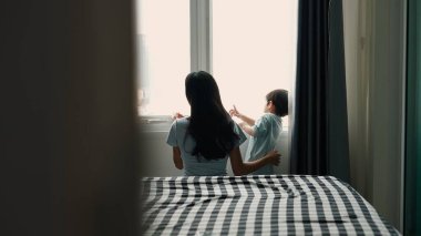 Anne kucaklaması evlat, yatak odasının penceresinden şehrin manzarasını seyrediyor.