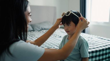 Mutlu anne güneşli bir günde dışarı çıkmaya hazırlanırken küçük oğluna güneş gözlüğü takıyor.