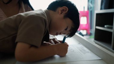 Çizimlerine odaklanan genç çocuk, çocukluk yaratıcılığının ve öğrenmenin neşesini gözler önüne seriyor.