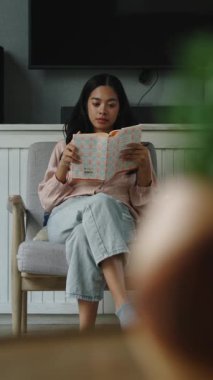 Minimalist yaşam alanının geniş penceresinin yanında rahatça otururken rahat bir kadın kitap okuyor.