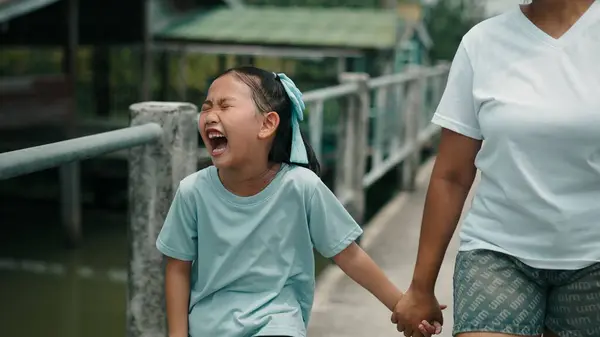 Ağlamaklı bir şekilde annesinin elini tutan çocuk ahşap köprü üzerinde dururken duygusal sıkıntı gösteriyor.