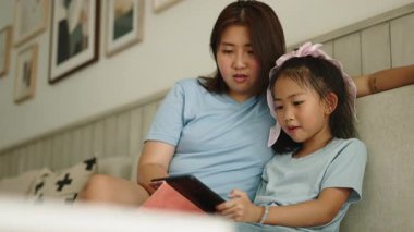 Kanepede dijital tableti paylaşan Asyalı genç anne ve kız - 4K Yatay
