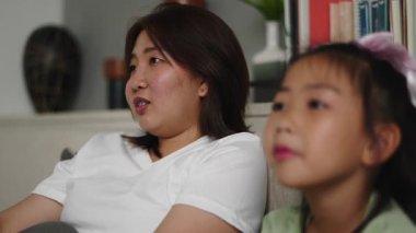 Anne ve kızı oturma odasında televizyon izleyerek eğleniyorlar - 4K Yatay