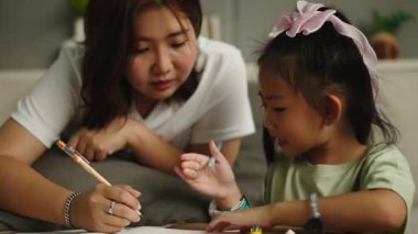 Asyalı bir anne, genç kızına evde 4K Yatay Not Defteri 'ni öğrenmesi ve yazması için yardım eder.