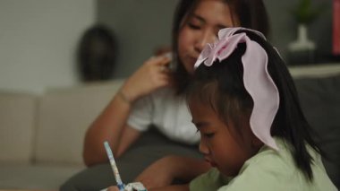 Genç Asyalı anne evde kızına yazma alıştırmasında yardım ediyor - 4K Yatay