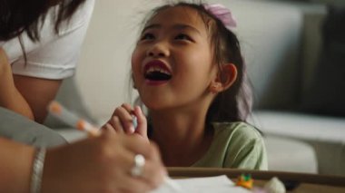 Mutlu Asyalı kız annesinin yardımıyla bir deftere yazıp çiziyor - 4K Yatay