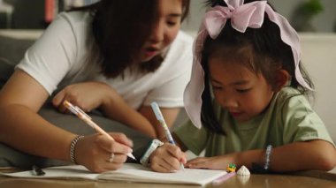 Asyalı bir anne, genç kızına pozitif bir öğrenme deneyimini teşvik etmek için ev ödevinde yardım eder - 4K Yatay