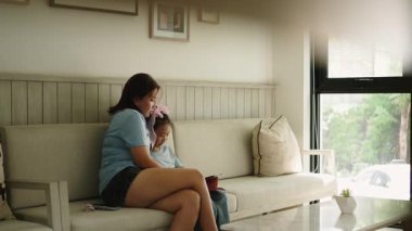 Genç bir Asyalı anne kızıyla birlikte oturma odasındaki bir kanepede tablet kullanırken - 4K Yatay