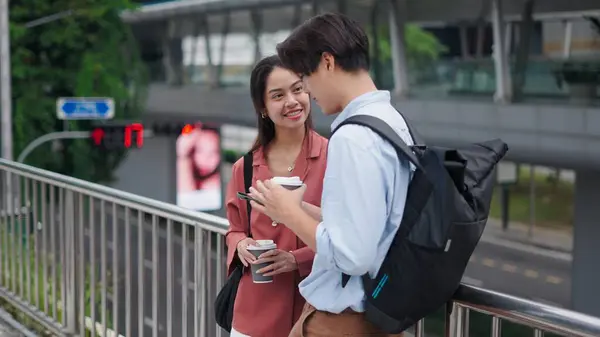İki genç profesyonel şehirde yaya köprüsünde dikilirken sohbet ediyor ve kahve içiyorlar.