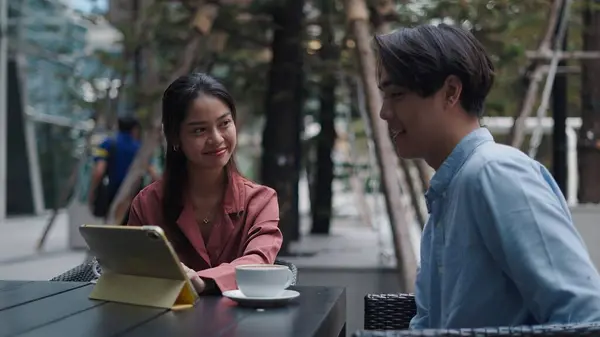 Proje detaylarını tartışan genç profesyoneller güneşli açık kafede kahve içerken tablet üzerinde uzaktan çalışıyor.