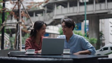 İş arkadaşları laptopta iş birliği yapıyor, açık kafede kahve yudumluyor ve iş projesini tartışıyorlar.
