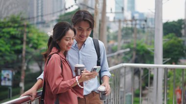 İki genç Asyalı profesyonel kahve içiyor ve bir şehir üst geçidinde akıllı telefon kullanıyorlar.