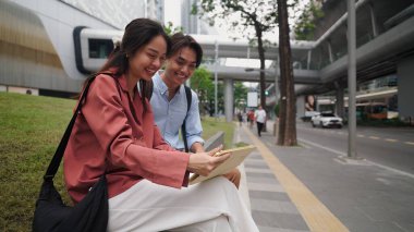 İki genç girişimci, modern bir şehirde çalışırken tablet kullanıyor ve gülümsüyor.