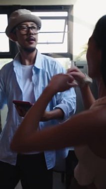 Genç Asyalı çift dans ediyor ve akıllı telefon kullanarak modern mutfaklarında eğleniyorlar.