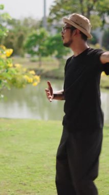 Asyalı bir adam göl kenarındaki FullHD Dikey Parkı 'nda yavaş dans adımları atıyor.