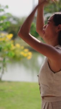Genç Asyalı mutlu bir kadın göl kenarındaki parkta dans ediyor ve eğleniyor.