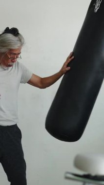 Uzun saçlı, Asyalı son sınıf öğrencisi, pencerede kum torbasıyla antrenman yapıyor.