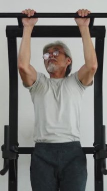 Asyalı son sınıf öğrencisi dayanıklılığını ve formunu korumak için duvara monte edilmiş bir barfiks çekiyor.