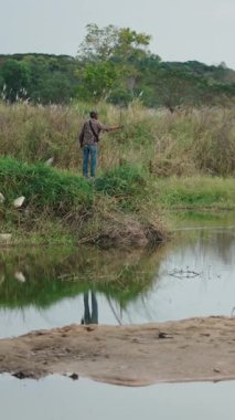 Balıkçı halatını sakin bir nehre atar. Yansıması onu sudaki yansıtır. Etrafı yemyeşil bitki örtüsü ve dalgalı tepelerle çevrilidir.