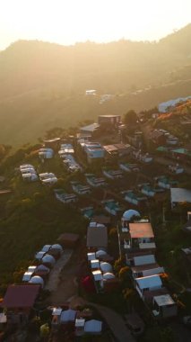 Gün batımıyla aydınlanan bir dağ yamacındaki tatil köyü FullHD Dikey