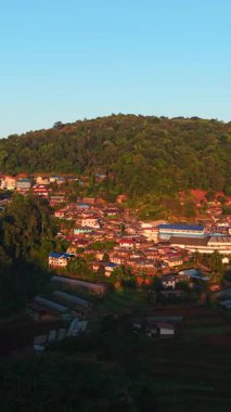 Güneş batarken dağların yakınındaki bir drondan görülen sessiz köy - FullHD Dikey