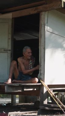 Ahşap bir kulübenin kapısında oturan çok delago Asyalı son sınıf öğrencisi tavukları besler.