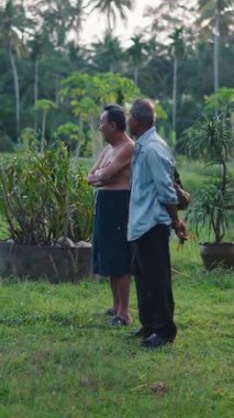 İki çiftçi tropikal bir bahçede durup Tayland 'daki mahsullerini ve palmiyelerini izliyorlar.