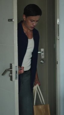 Market poşetleri taşıyan genç bir adam, alışveriş yaptıktan sonra mutfağa giriyor. Bağımsız Yaşamı temsil ediyor.