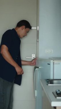 Genç Asyalı adam mutfak dolabında taze erzak depoluyor, FullHD dikey.