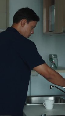 Asyalı Adam, Samrtphone 'unun yanında minimalist bir mutfakta sabah kahvesi hazırlıyor.