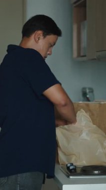 Mutfak tezgahında duran genç adam, sürdürülebilir bir kese kağıdından taze paketleri dikkatlice açıyor.