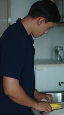 Sağlıklı bir yaşam tarzı olan minimalist ve temiz mutfak tezgahında olgun bir muzu dikkatlice soyan genç adam.