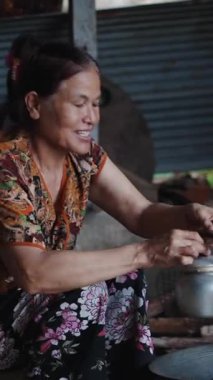 Yaşlı kadın ahşap bir ocakta metal bir çaydanlıkta su kaynatıyor geleneksel bir ortamda, FullHD dikey