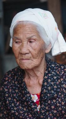 Başörtüsü takan düşünceli yaşlı bir kadının portresi kırsal alanda çalışan başka bir kadını izliyor.