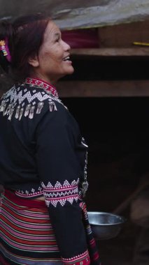 Geleneksel giysiler içindeki yaşlı Taylandlı kadın geleneksel ahşap bir evin önünde kaseyi tutarken mutlu bir şekilde gülümsüyor.