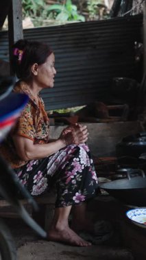 Taylandlı son sınıf öğrencisi, yalınayak, mütevazı bir kulübede geleneksel ahşap bir ateşte çay hazırlıyor.