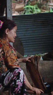 Köy mutfağında odun kesen deneyimli yaşlı kadın geleneksel yemek pişirme yakıtı FullHD dikey