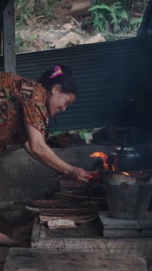 Köy ortamında geleneksel yemek pişirme yöntemlerini gösteren bir odun sobasında yemek hazırlayan yaşlı kadın.