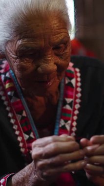 Yaşlı bir Asyalı kadın titizlikle iğnenin ucuna iplik geçirip geleneksel Tayland seti FullHD dikey tekstil üzerinde çalışıyor.